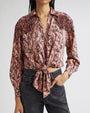 Person wearing a long-sleeved paisley-patterned shirt in pink, and black with fringe detailing on the shoulders, tied at the waist, paired with dark gray jeans.