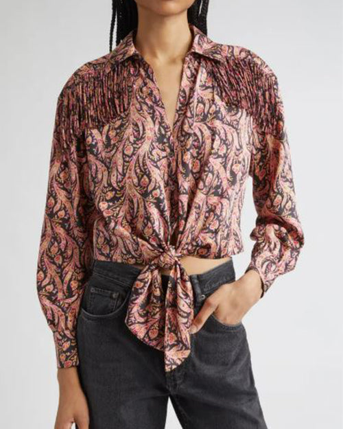 Person wearing a long-sleeved paisley-patterned shirt in pink, and black with fringe detailing on the shoulders, tied at the waist, paired with dark gray jeans.