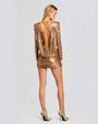 A back view of a golden metallic dress with long sleeves and low plunge back. The dress ends mid thigh and has a ruched bottom.