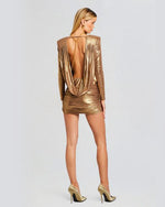 A back view of a golden metallic dress with long sleeves and low plunge back. The dress ends mid thigh and has a ruched bottom.