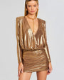 A close up of a golden metallic dress with long sleeves and low plunge V neck. The shoulders have slight structure for a boxy shoulder effect. The dress is styled with gold chunky jewelry.