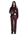 Person standing and facing forward, wearing a dark red sweater with white star patterns and matching dark red pants, holding a black handbag in the left hand and wearing black shoes. 
