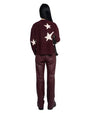 Person standing with their back to the camera, wearing a dark maroon sweater with white star patterns on the back and sleeves, paired with matching maroon pants. They have long black hair and are carrying a black shoulder bag.