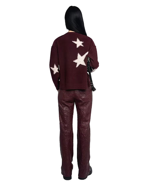 Person standing with their back to the camera, wearing a dark maroon sweater with white star patterns on the back and sleeves, paired with matching maroon pants. They have long black hair and are carrying a black shoulder bag.