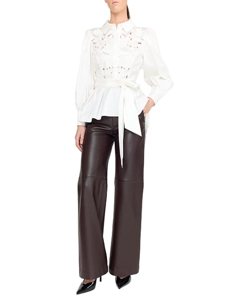 A person wearing a white blouse with intricate lace detailing and puffed sleeves, paired with high-waisted, wide-leg brown leather pants and black pointed-toe shoes.