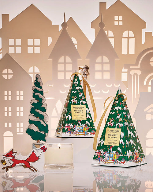 Two Christmas tree-shaped boxes with festive designs on a decorative background with houses and a fox.