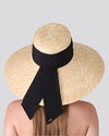 Person wearing a wide-brimmed straw hat with a black ribbon bow, viewed from behind against a light background.