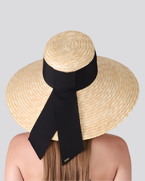 Person wearing a wide-brimmed straw hat with a black ribbon bow, viewed from behind against a light background.