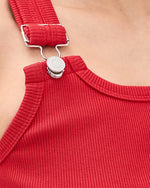 A closeup view of an adjustable buckle strap with silver buttons on a bright red tank top.