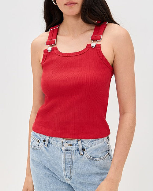A person wearing a bright red tank top with adjustable buckle straps and light blue jeans.