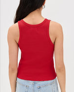 The backside view of a person wearing a bright red tank top with adjustable buckle straps and light blue jeans.