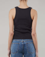 The backside view of a person wearing a navy tank top with adjustable buckle straps and blue jeans.