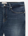 Close-up of dark blue denim jeans, silver button closure, and contrast orange stitching. Includes small watch pocket and subtle color variations.