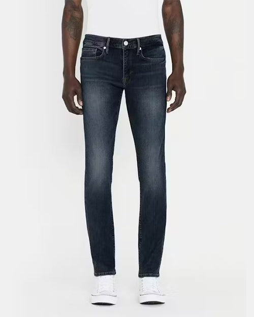 A pair of dark blue denim jeans with a faded effect around the thigh and knee area. The jeans have silver hardware above pockets and the button. The jeans have a fitted cut, visible stitching, and are styled with a black belt, white shirt and white sneakers.