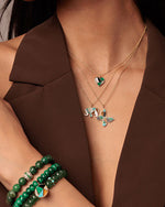 A close-up image of a person wearing a brown V-neck garment adorned with multiple pieces of jewelry.