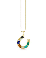 A gold necklace with a pendant in the shape of a horseshoe. The horseshoe pendant features an alternating pattern of dark blue, black, and green gemstones sections, interspersed with small round diamonds that add sparkle to the design.