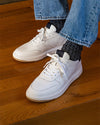White sneakers worn with blue jeans on a wooden floor
