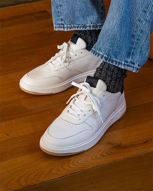White sneakers worn with blue jeans on a wooden floor