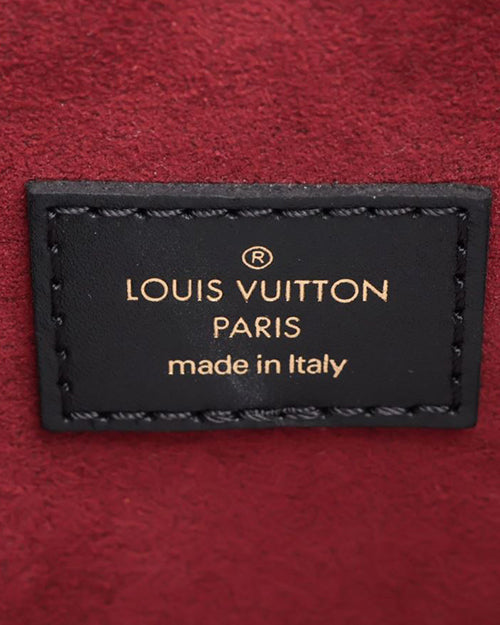 The interior of a designer bag with red material. The image depicts a close-up of a black rectangular label with gold lettering.