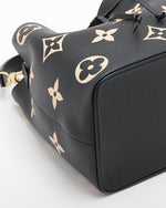 Bottom view of a designer handbag, the leather has a matte finish, and a distinctive pattern of beige and white monograms. The handle has a gold clasp and the bottom has a square support at the bottom of the bag. 