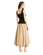 Back view of a  person standing in front of a plain background wearing a sleeveless dress with a black bodice and a voluminous, ankle-length beige skirt. They are also wearing beige open-toe sandals.
