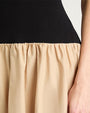 Close-up of a person wearing a dress with a fitted black top and a gathered beige skirt. The person's right hand rests against the beige fabric.