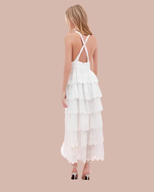 Back view of model wearing white dress with criss crossed straps, multiple layers and patterns, paired with light-colored sandals.