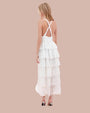 Back view of model wearing white dress with criss crossed straps, multiple layers and patterns, paired with light-colored sandals.