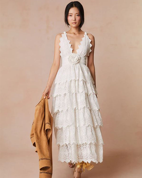 Model wearing a detailed white halter dress with multiple layers and patterns, paired with light-colored sandals.