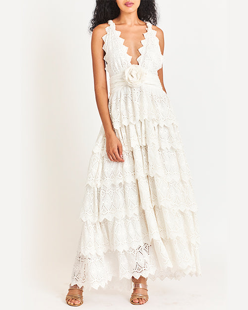 Model wearing a detailed white halter dress with multiple layers and patterns, paired with light-colored sandals.