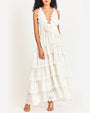 Model wearing a detailed white halter dress with multiple layers and patterns, paired with light-colored sandals.