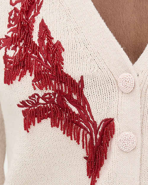 A close up of a cream cardigan with red beaded and embroider design and button details