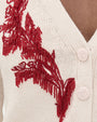 A close up of a cream cardigan with red beaded and embroider design and button details