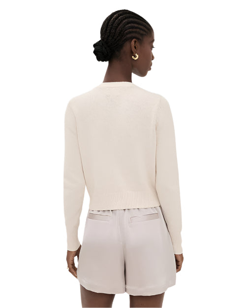 Back view of a woman wearing a beige sweater and shorts on a white background