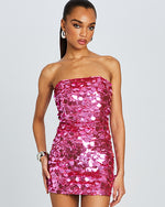 A close up of a bodycon mini dress adorned with shimmering, overlapping pink sequins. The dress features a straight neckline and is fitted throughout, highlighting a figure-hugging silhouette. The sequins catch the light at various angles, creating a sparkling effect across the entire garment.