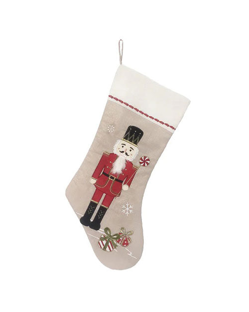 A beige Christmas stocking features a nutcracker in a red uniform, accented by snowflakes and gift boxes, creating a festive and whimsical holiday tone.