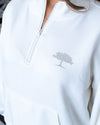 A close-up of a white quarter zip with white zipper and grey tree silhouette logo on right chest.