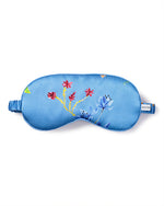 A blue sleeping mask with a floral pattern featuring red, blue, and yellow flowers and green leaves. The mask has an elastic band to secure around the head and a small tag with the brand name.