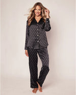 A model in a black silk pajama set with a long-sleeved button-up shirt and matching pants. The set features an all-over print of small white motifs. The shirt has a notched collar, a pocket on the left breast.