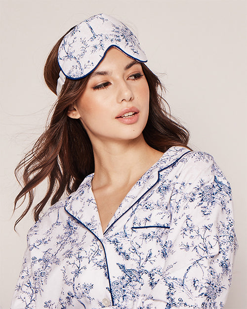 A model wearing a white and blue floral-patterned sleeping mask. The mask has an adjustable white strap for size adjustment. Model is wearing matching pajama top.