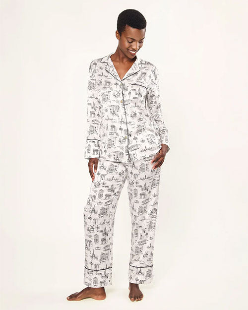 Person wearing a white pajama set with black piping and an all-over print of various buildings and landmarks. The set includes a long-sleeved, collared, button-down top and full-length, relaxed-fit pants.