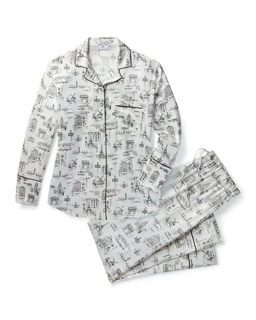 White pajama set with black architectural and cityscape print, featuring a long-sleeved button-up shirt with black piping along the collar, placket, cuffs, and pocket edges, and matching pants with an elastic waistband and drawstring.