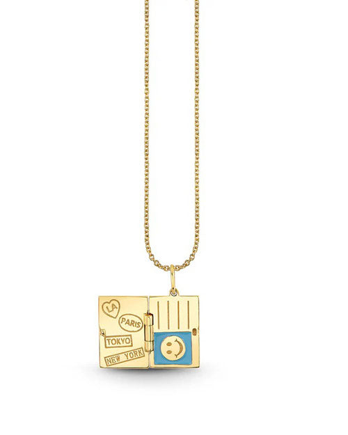 A gold necklace with a pendant designed to resemble an open passport. The left side of the pendant features engraved iconic city names such as “Paris,” “Tokyo,” and “New York". The right side displays vertical lines mimicking the pages of a passport, with a circular stamp-like design in the center. The charm conveys a theme of travel and adventure.