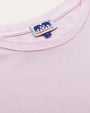 Close-up of a light pink crew neck t-shirt with a small white and navy rectangular label stitched at the center of the collar. The label features an elephant silhouette and logo lettering.