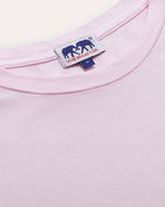 Close-up of a light pink crew neck t-shirt with a small white and navy rectangular label stitched at the center of the collar. The label features an elephant silhouette and logo lettering.