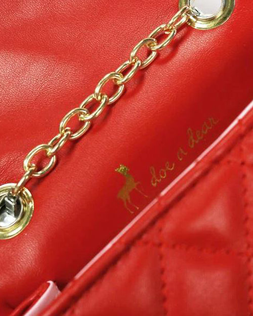 Interior close-up with red leather surface and gold chain embellishment. Circular links and "doe a deer" phrase with deer silhouette in gold.