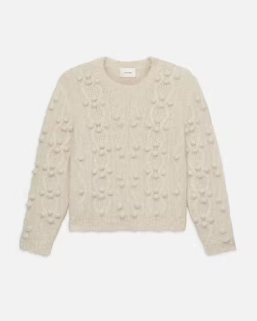 A cream-colored cable knit sweater with a crew neckline and long sleeves, displayed against a plain background. The sweater features intricate patterns of braided knits and various textures that create a cozy and warm appearance.