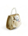 A side view of small handbag featuring a pearl handle. The bag is primarily gold in color with a white teddy bear applique on the front, adorned with a small blue bow, white ruffled dress and holding what appears to be a pink bouquet. 