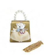 A small handbag featuring a pearl handle and an attached gold chain. The bag is primarily gold in color with a white teddy bear applique on the front, adorned with a small blue bow, white ruffled dress and holding what appears to be a pink bouquet. 