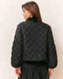 Back view of a black quilted jacket featuring a diamond-pattern stitch design, long sleeves, and a straight hem, paired with a black mini skirt.